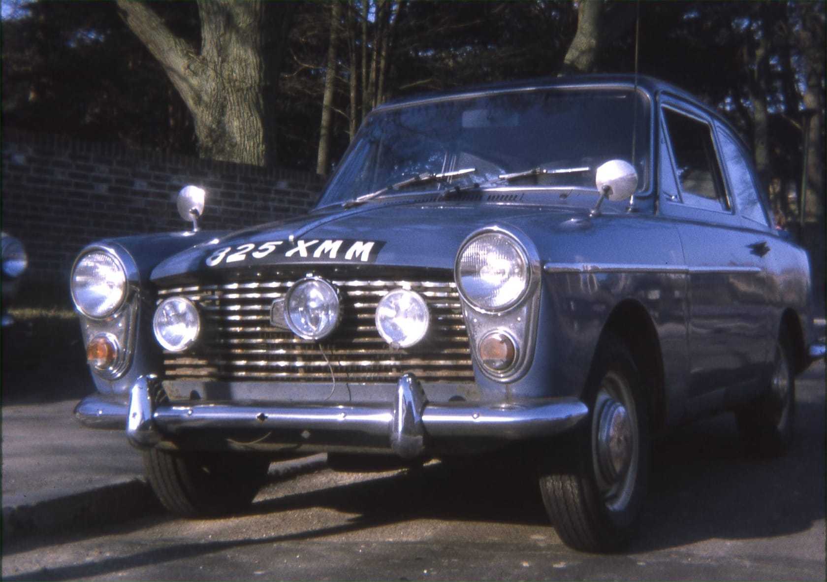 A period photograph of a pale blue Austin A40 Farina with auxiliary spot lamps and the registration 325 XMM on its front plate