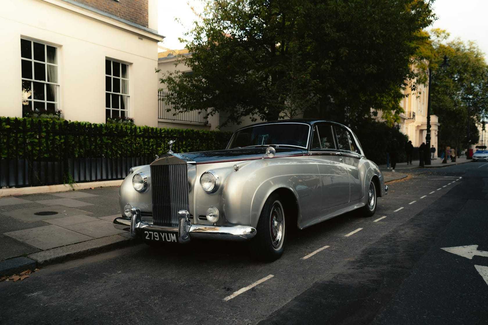 A silver Rolls-Royce Silver Cloud saloon, UK-registered, parked on a tree-lined London street