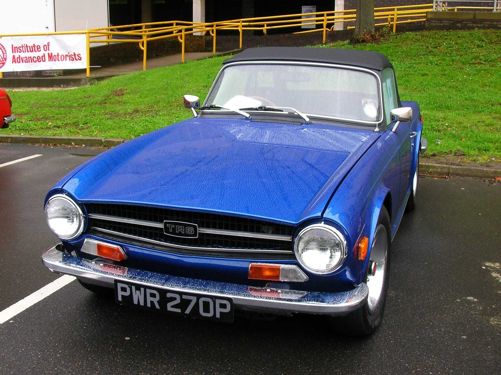 A blue Triumph TR6 with the top down, front three-quarter view on a road