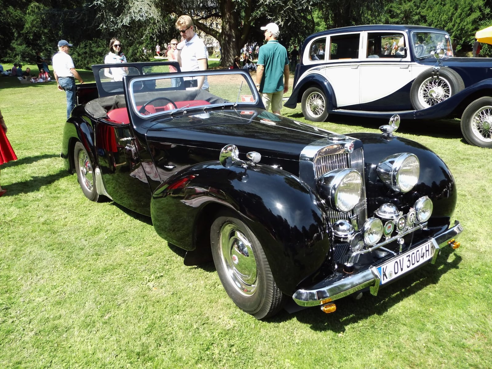 A black Triumph 1800 Roadster with red interior on grass at a classic car gathering, front three-quarter view