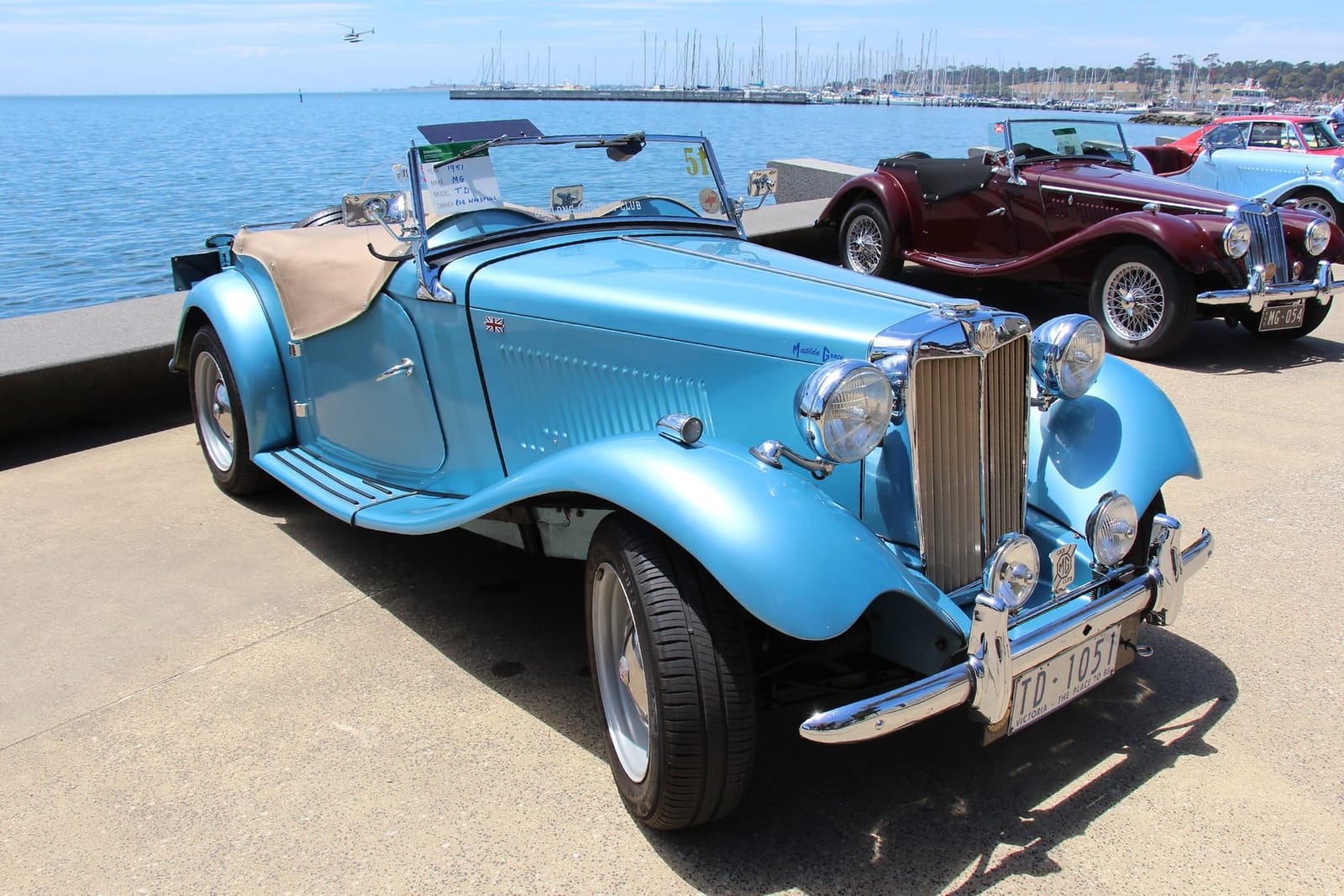 A light blue 1951 MG TD roadster with an American registration parked by a harbour