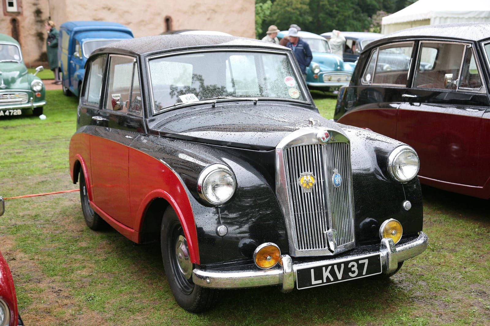 A black and red two-tone 1952 Triumph Mayflower on grass at a classic car show, front three-quarter view, UK registration LKV 37