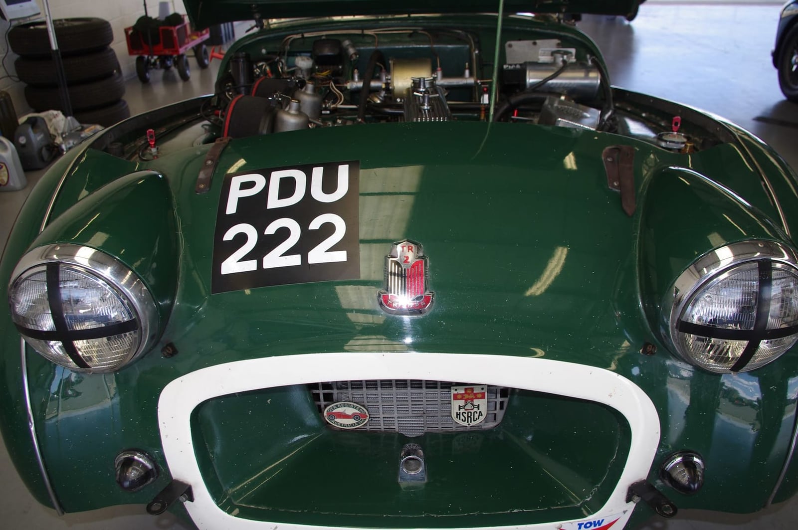 A green Triumph TR2 competition car with the bonnet open in the paddock, UK registration PDU 222