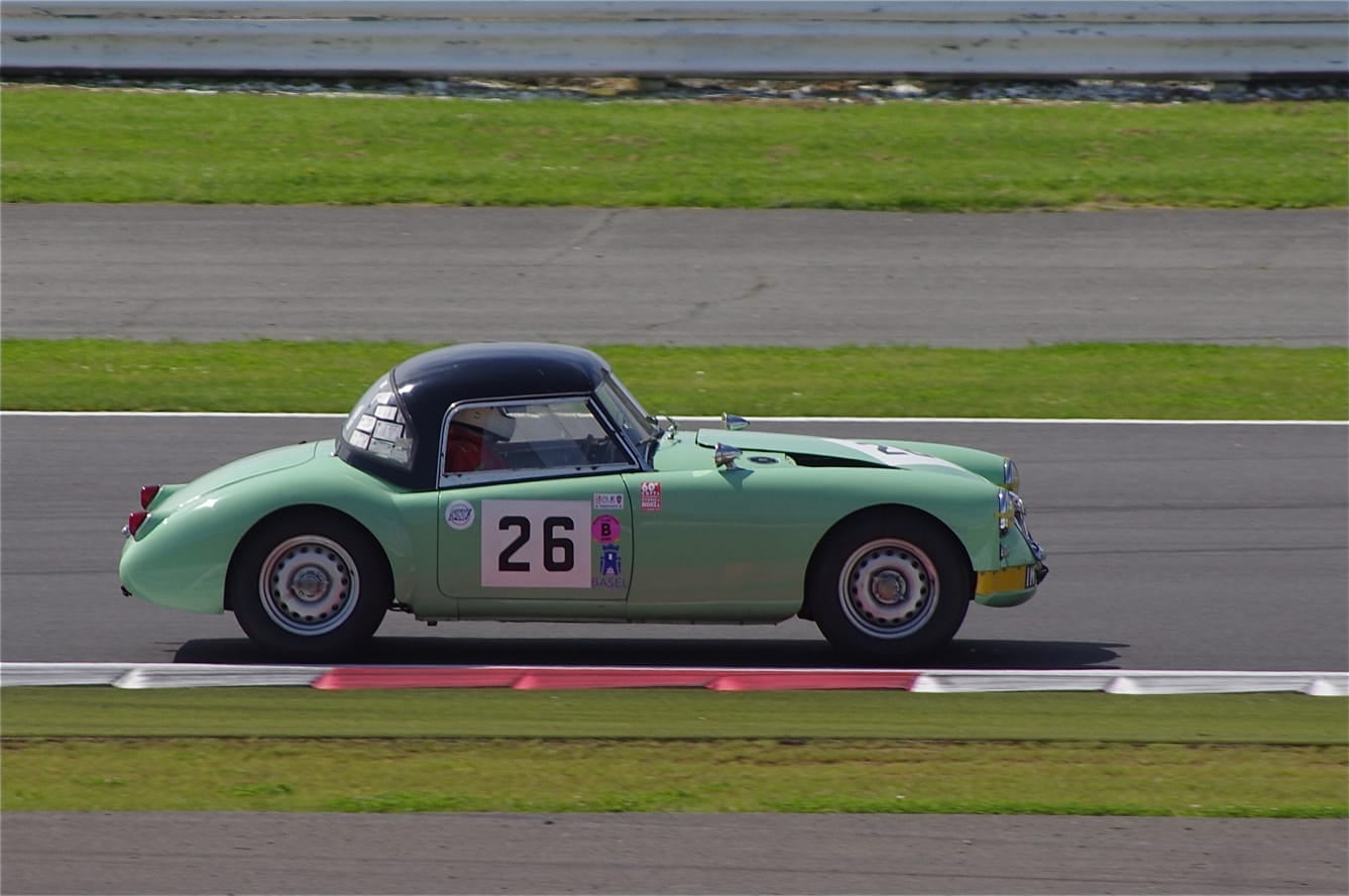 A green 1959 MGA Twin Cam coupé with race number 26 at speed on a racing circuit