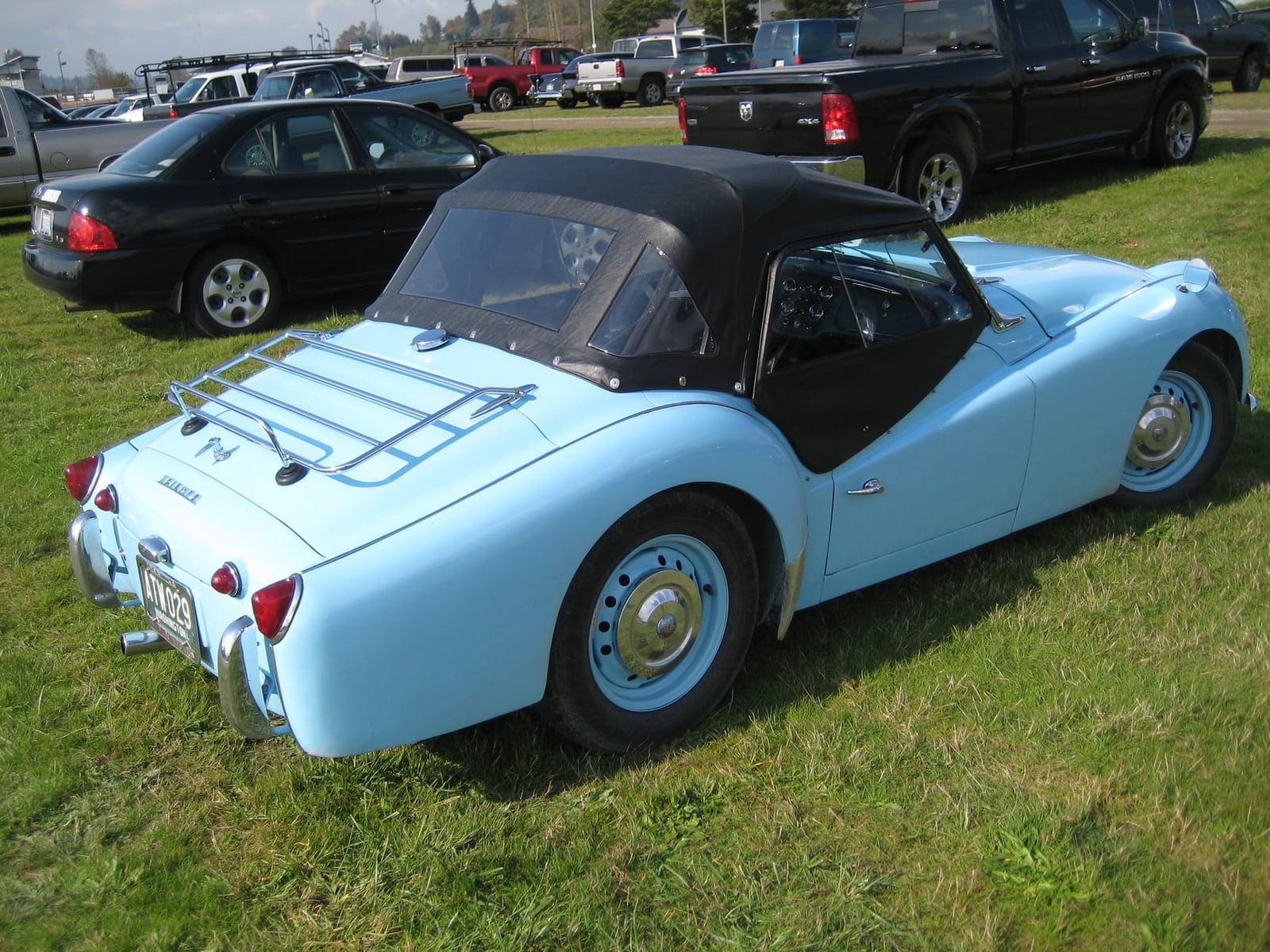 A pale blue Triumph TR3A with a chrome luggage rack on the boot lid, rear three-quarter view