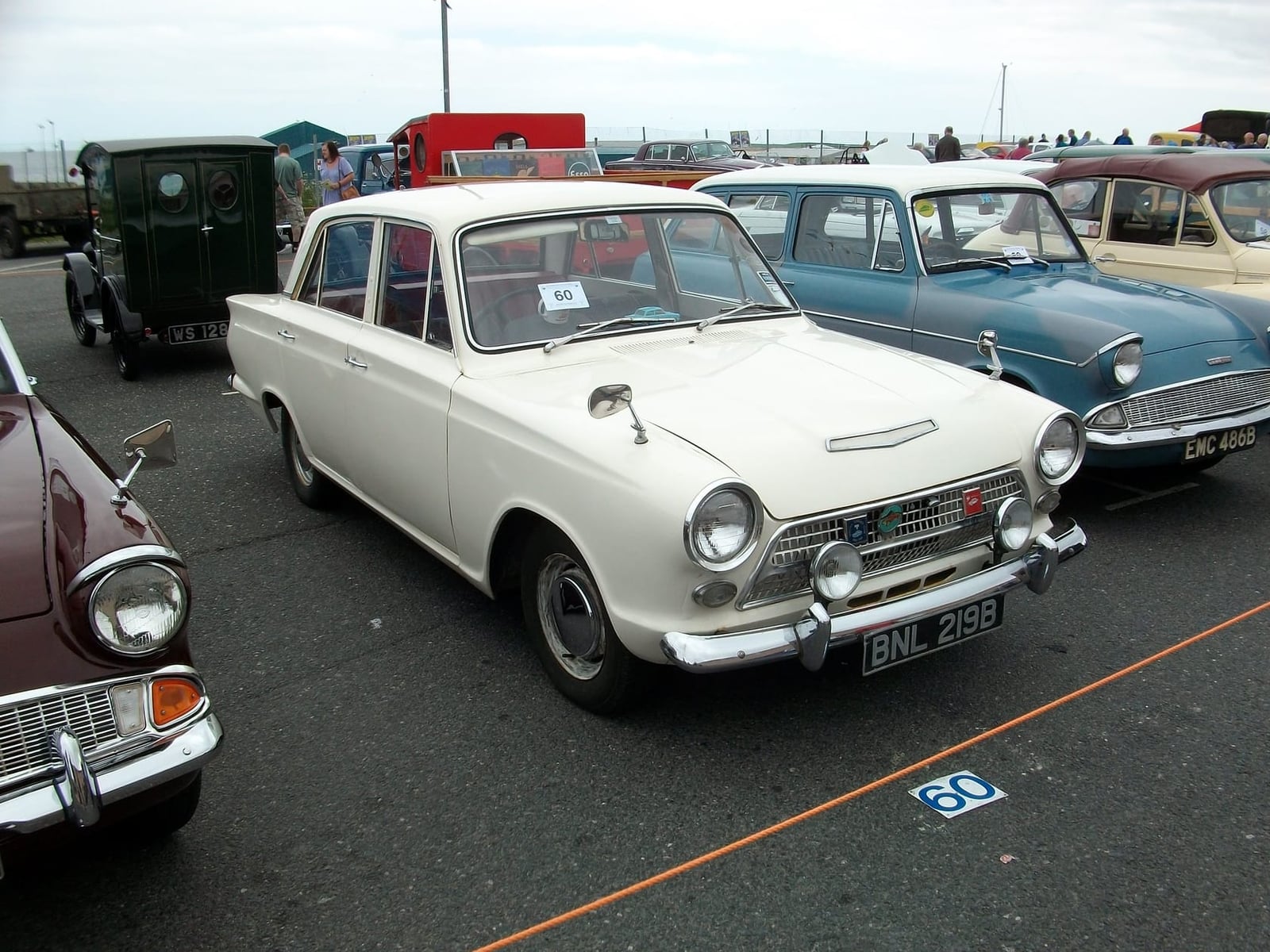 A cream 1964 Ford Cortina Mk1 at an outdoor classic car show, front three-quarter view, UK registration BNL 288B