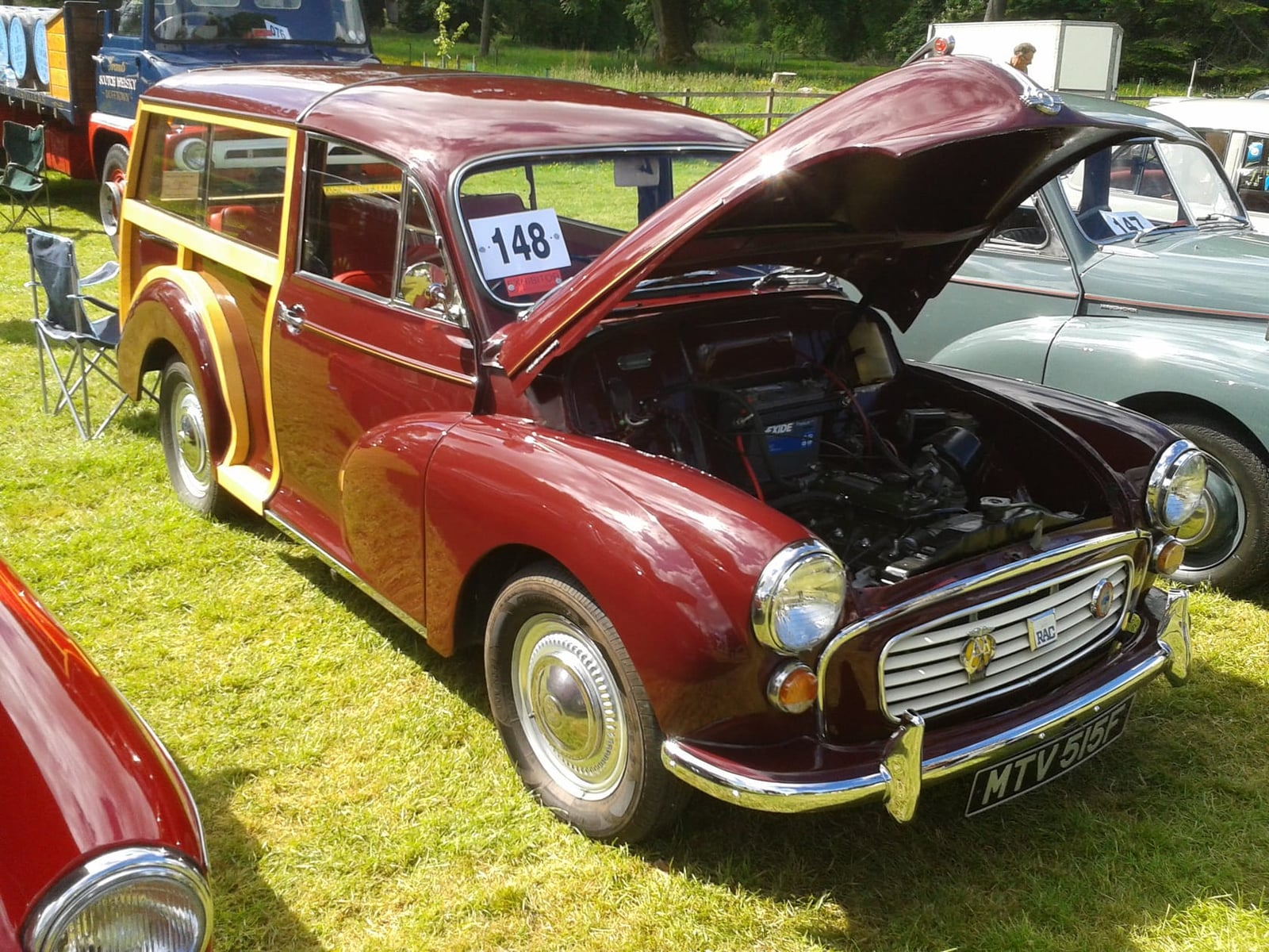 A maroon 1968 Morris Minor 1000 Traveller with its bonnet raised at a show, its ash frame and wood panels visible