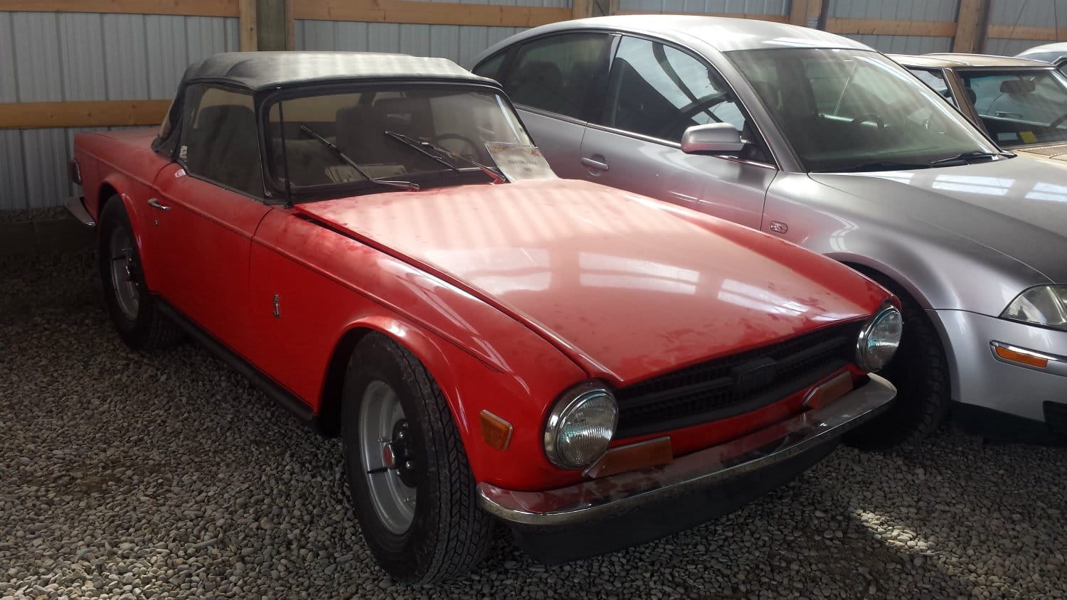 A red Triumph TR6 with the soft top up, front three-quarter view
