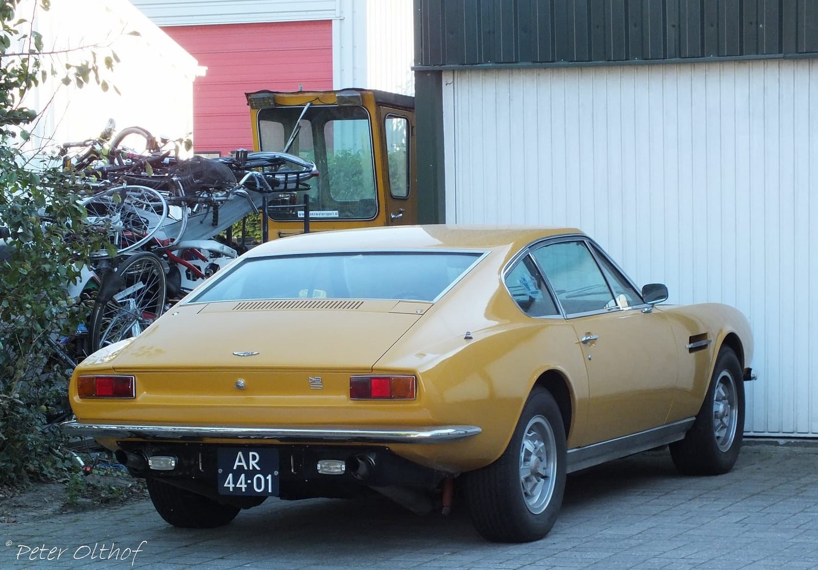 The rear of a yellow 1970 Aston Martin DBS with Dutch registration AR-44-01 parked by buildings