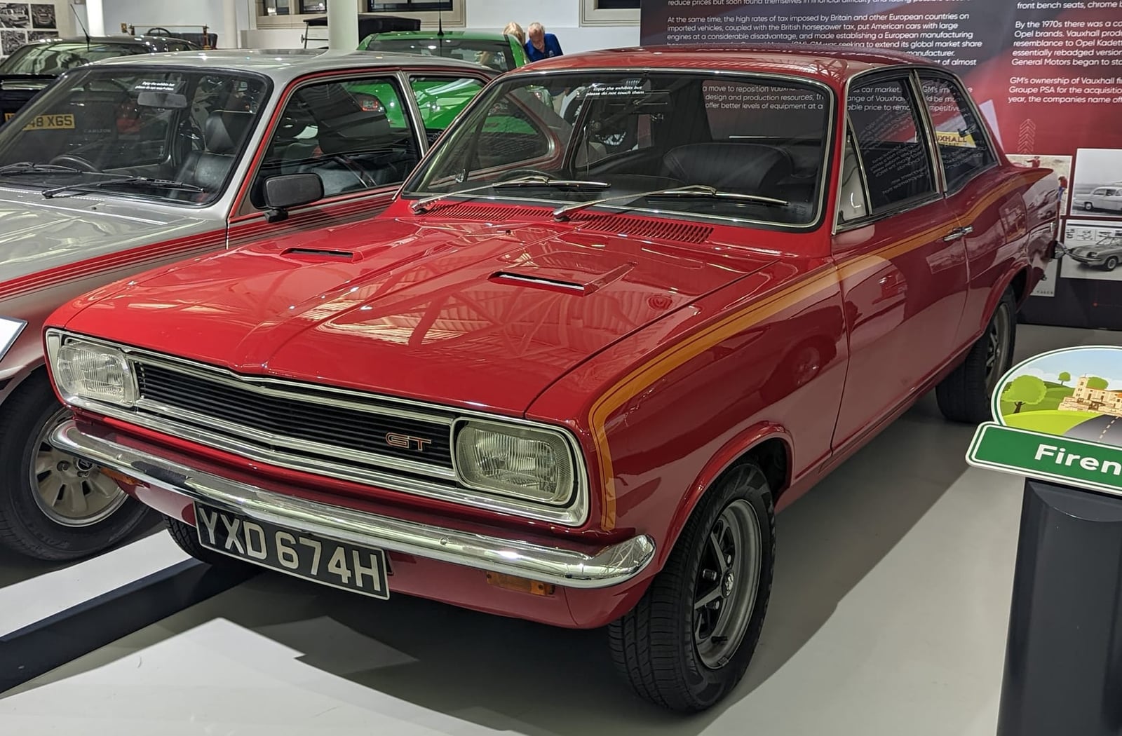 A red 1970 Vauxhall Viva GT with matt black bonnet on museum display, front three-quarter view, UK registration YXD 674H