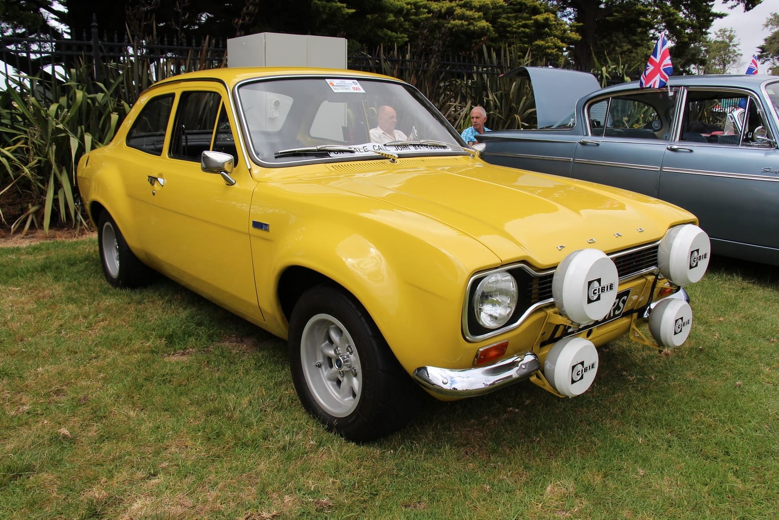 A yellow 1972 Ford Escort Mk1 RS1600 with rally spotlamps, parked on a show field