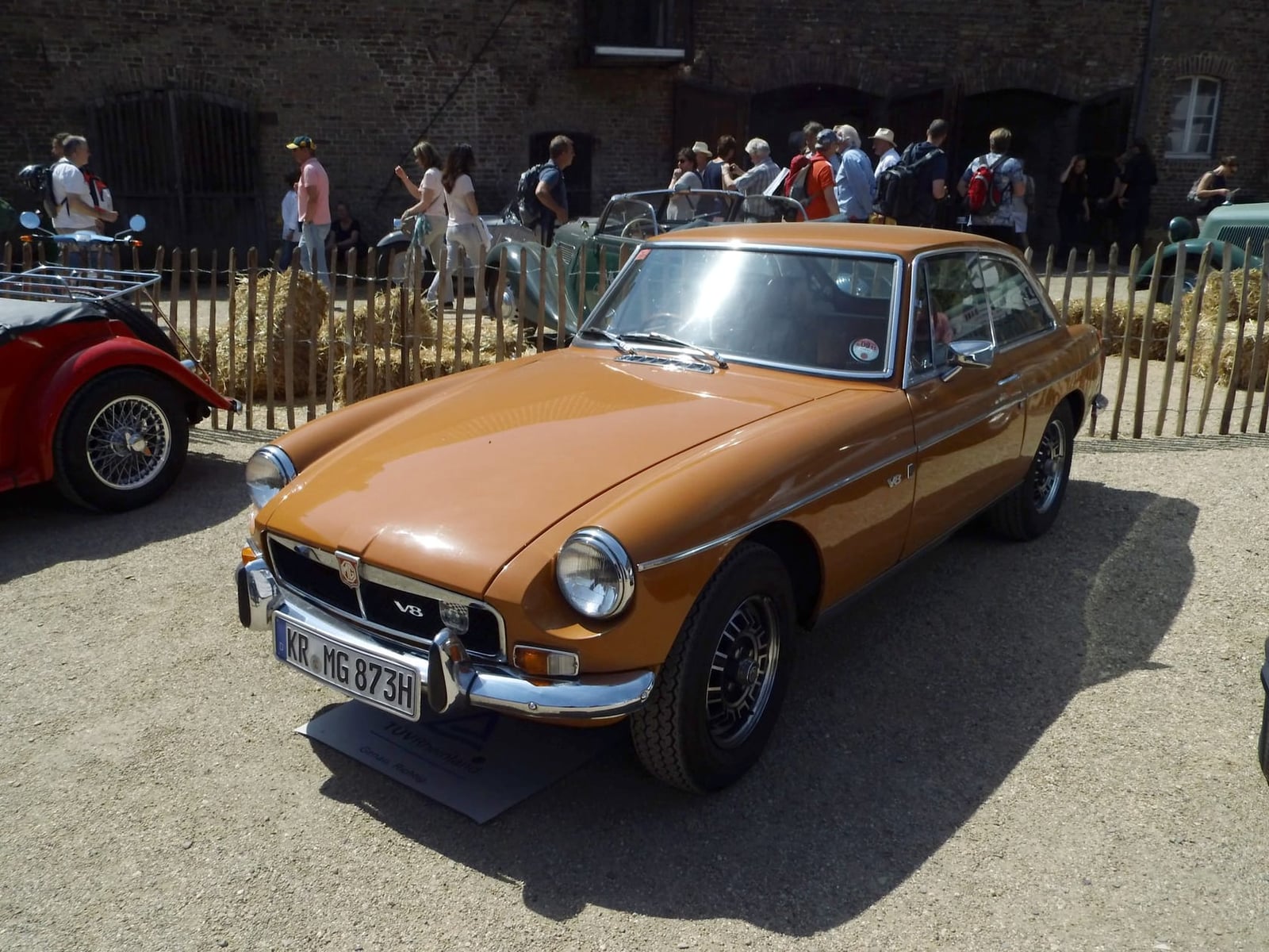 A 1973 MGB GT V8 in dark red at an outdoor classic car show