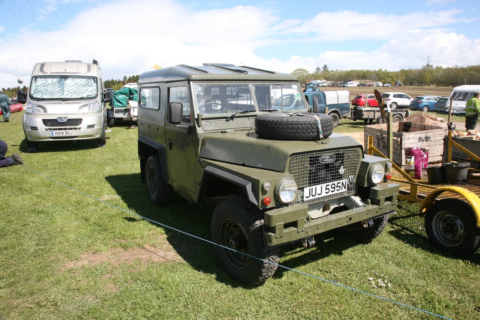 A green Land Rover Lightweight fitted with a hardtop on grass at a military vehicle rally, UK registration JUJ 595N