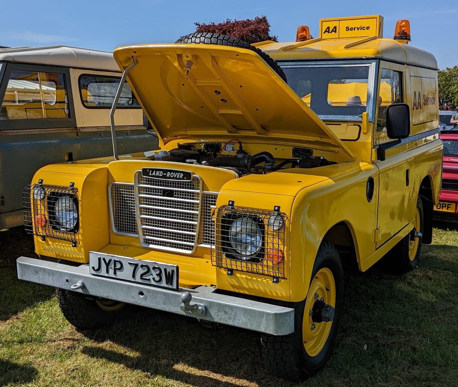 A yellow 1981 Land Rover Series III 88 in AA livery with its bonnet raised at a show