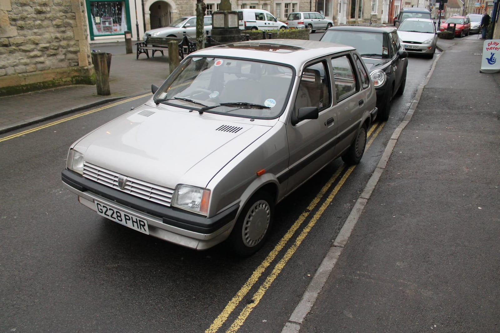 A silver 1989 Austin Metro Clubman parked at the kerb on a British street, front three-quarter view, UK registration C728 PHR