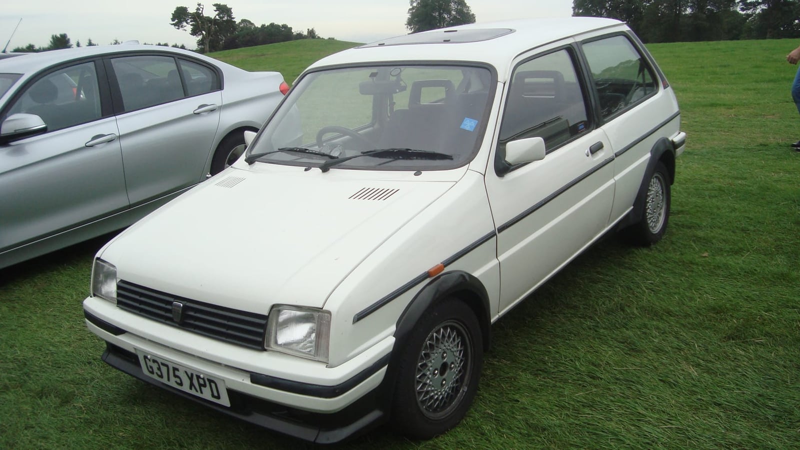 A white 1989 Rover Metro GTa on grass at a classic car show, front three-quarter view, UK registration G375 XPD