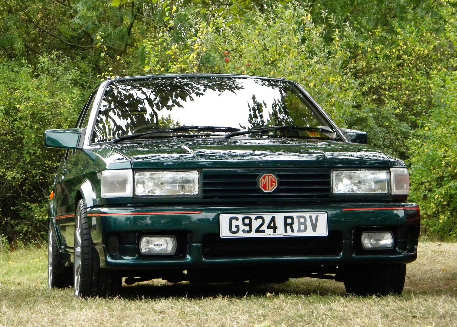 A British Racing Green 1990 MG Maestro Turbo with a UK registration parked in front of trees