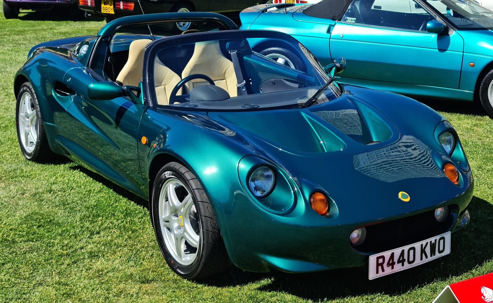 A British Racing Green 1998 Lotus Elise S1 with a tan interior and a UK registration on a show field, an Esprit behind
