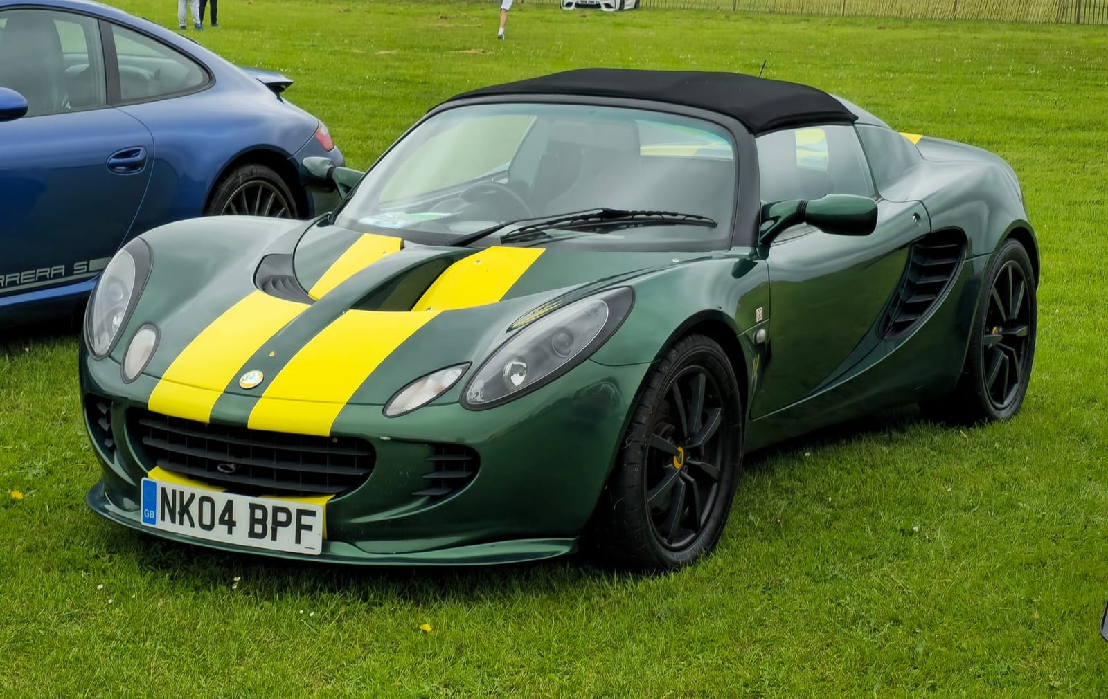 A dark green 2004 Lotus Elise 111S with a yellow centre stripe and a UK registration on a show field