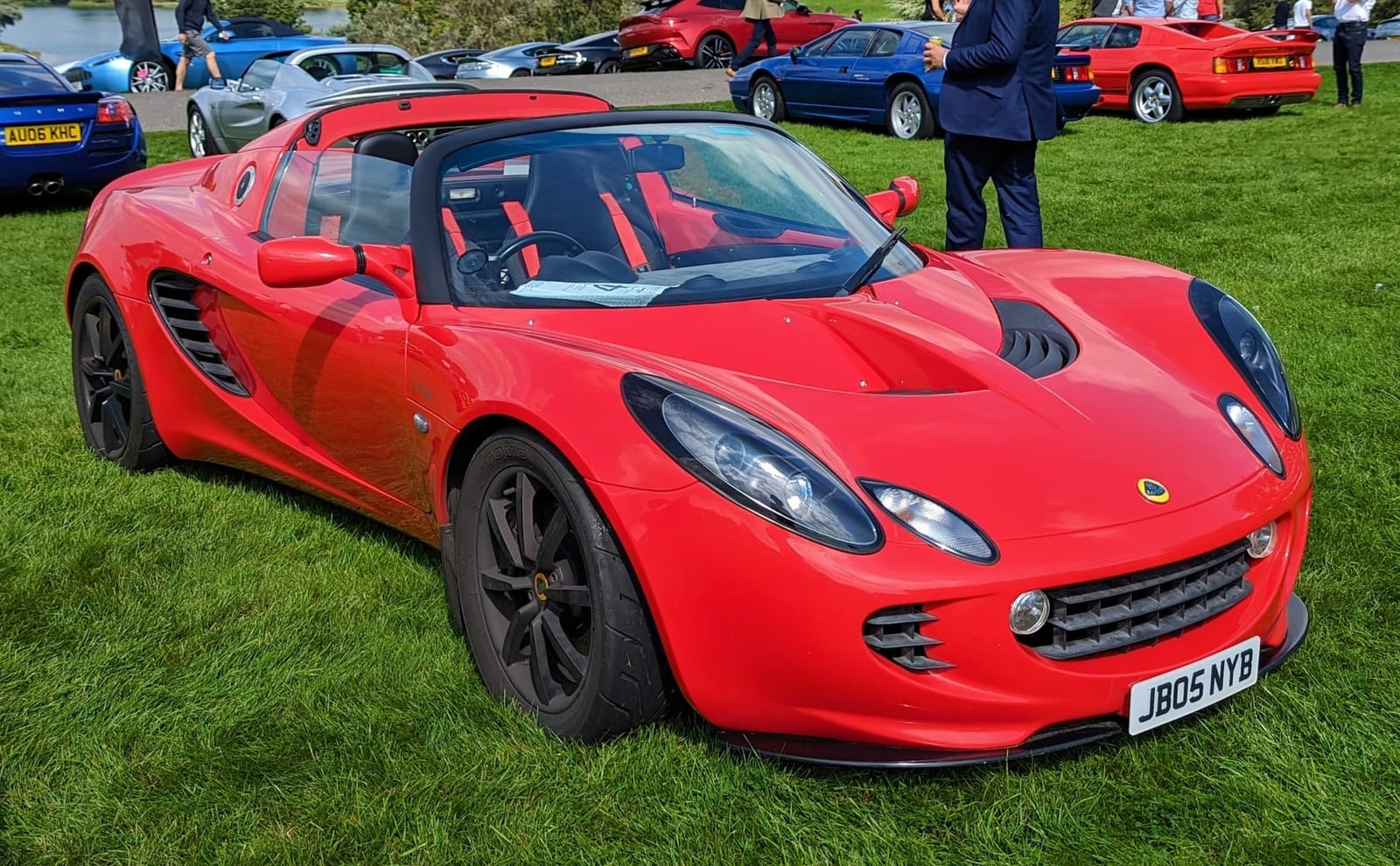 A red 2005 Lotus Elise 111S with black wheels and a UK registration on a show field