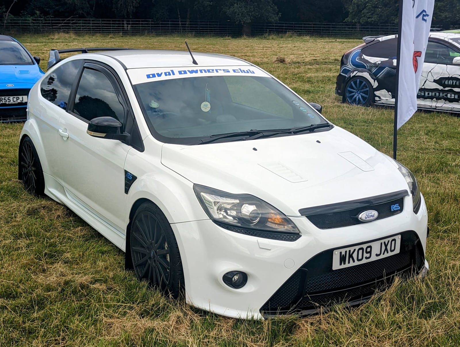 A white 2009 Ford Focus RS Mk2 with an owners' club sunstrip and a UK registration on a show field
