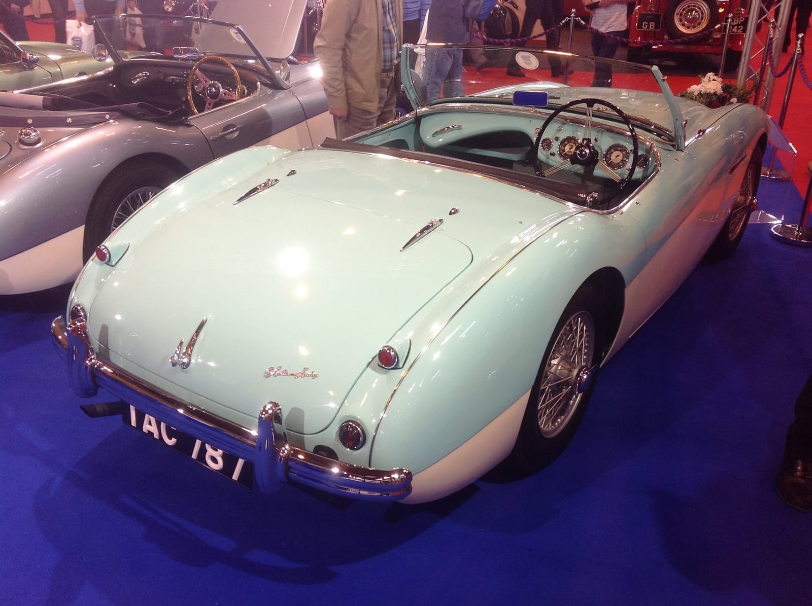The rear of a pale green and white 1955 Austin-Healey 100 with a UK registration on a motor show stand