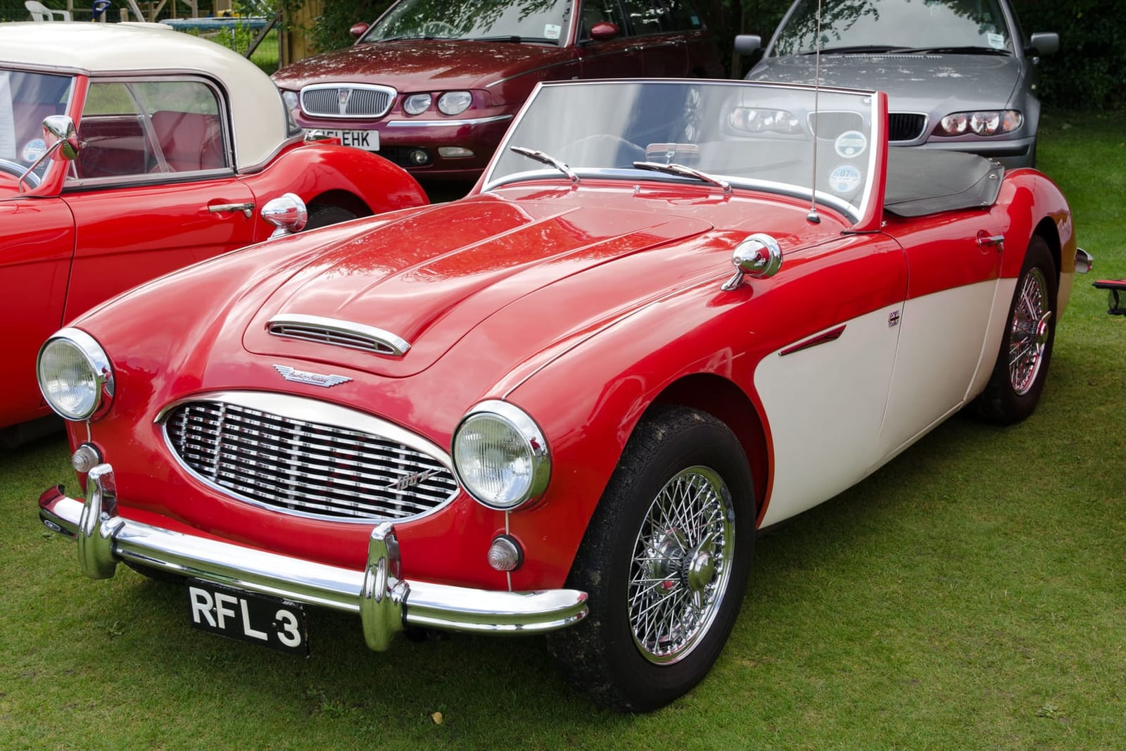 A red and white 1958 Austin-Healey 100/6 with a UK registration on a show field