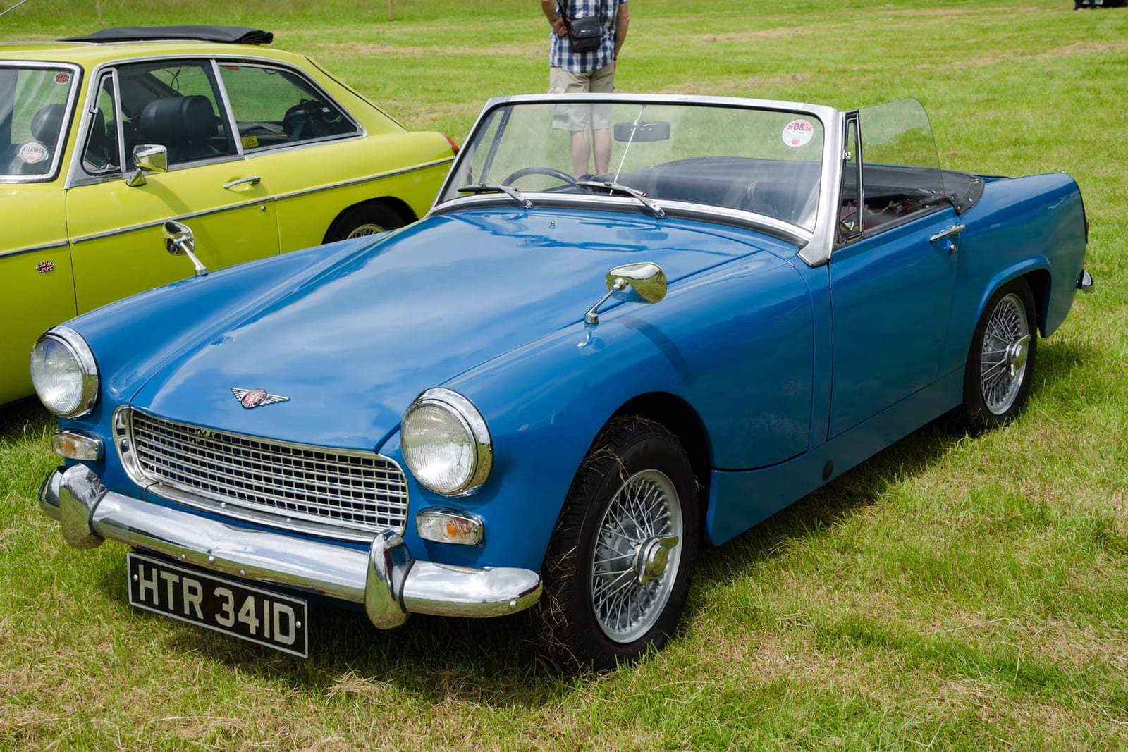 A blue 1966 Austin-Healey Sprite Mk III with wire wheels and a UK registration on a show field