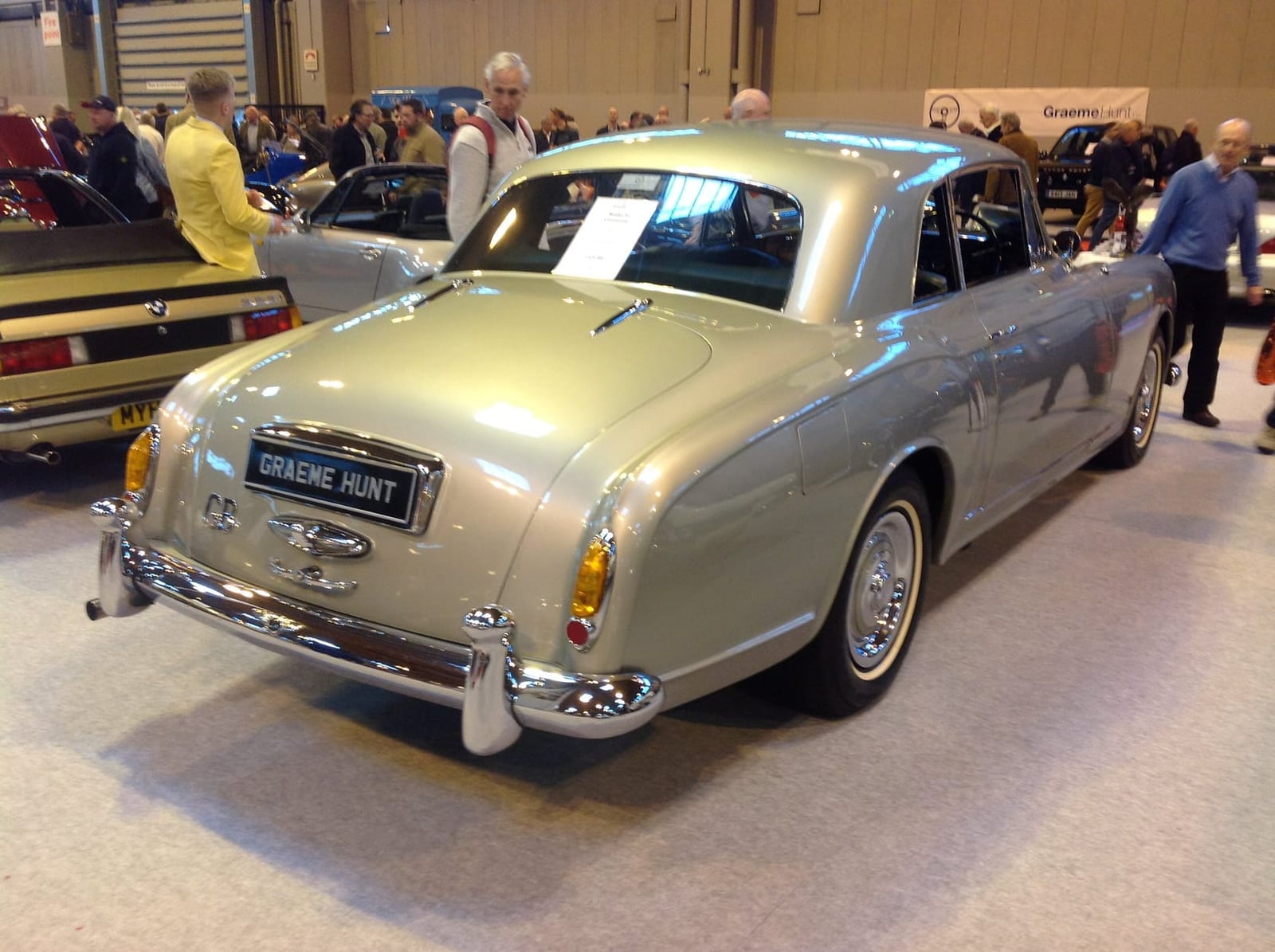 A gold 1956 Bentley S1 Continental fastback by Park Ward, rear three-quarter view at an indoor show