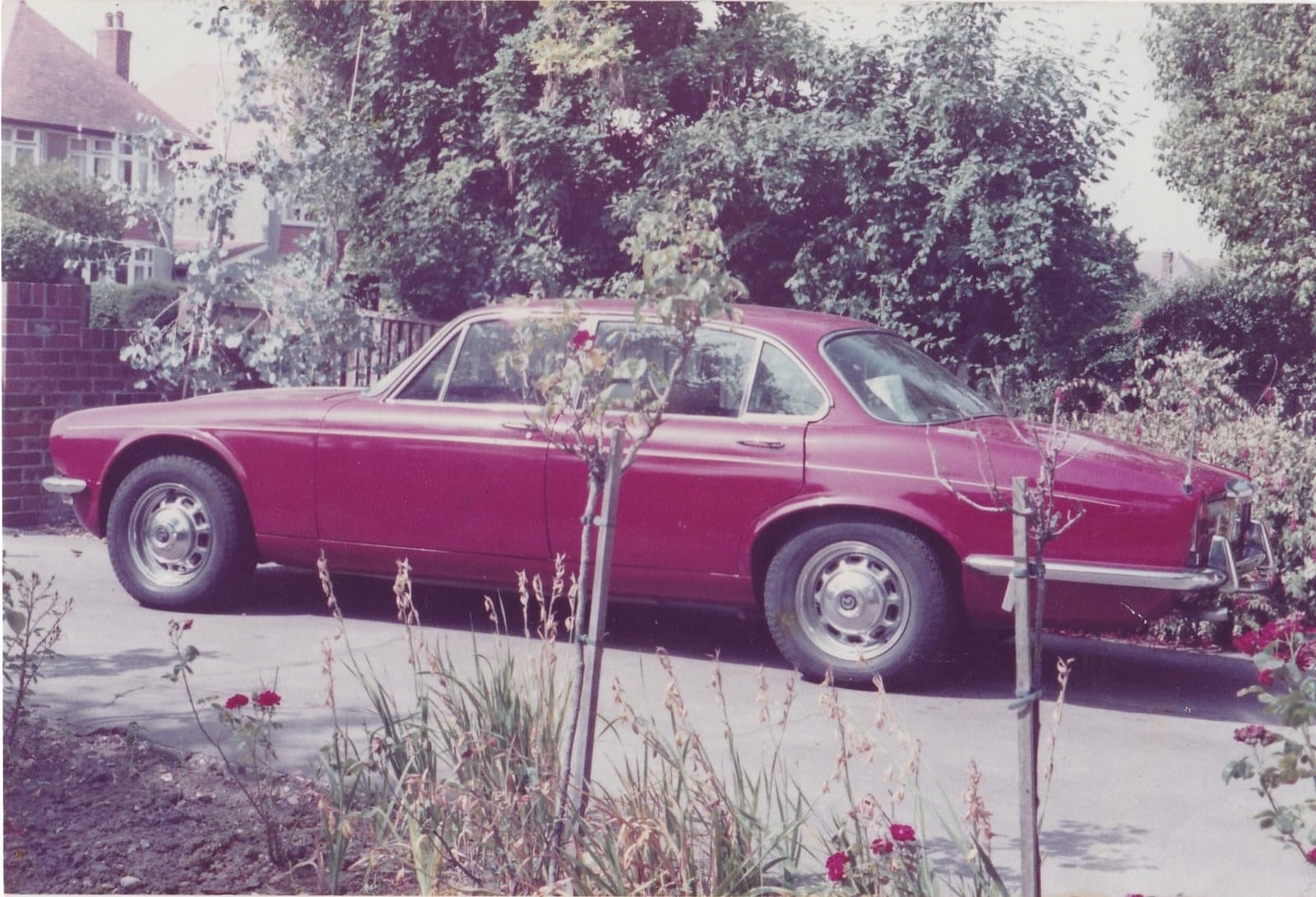 A faded period photograph of a maroon Jaguar XJ saloon parked outside a suburban British house