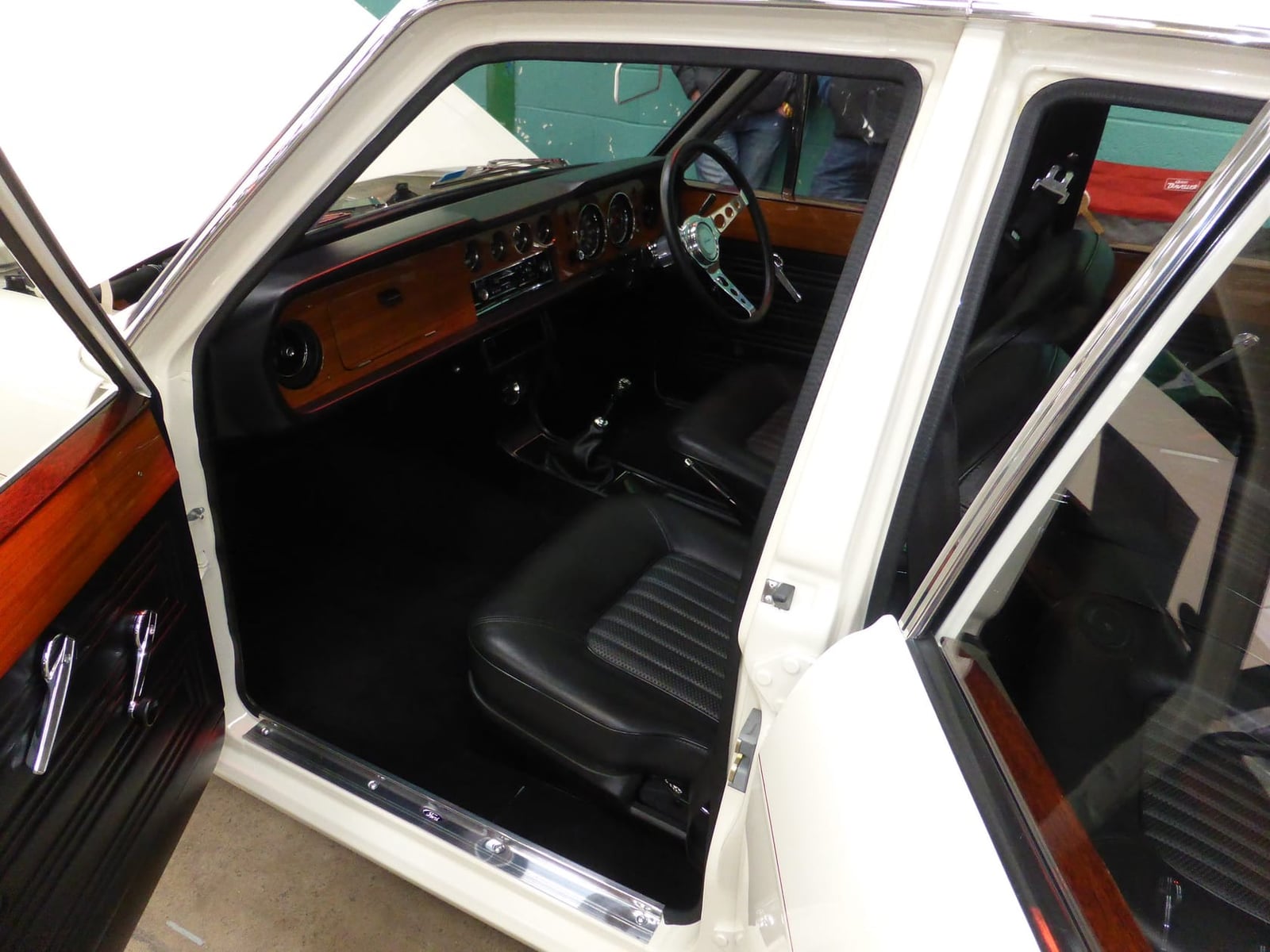 The interior of a Ford Cortina 1600E showing the wood-faced dashboard, door cappings and black seats
