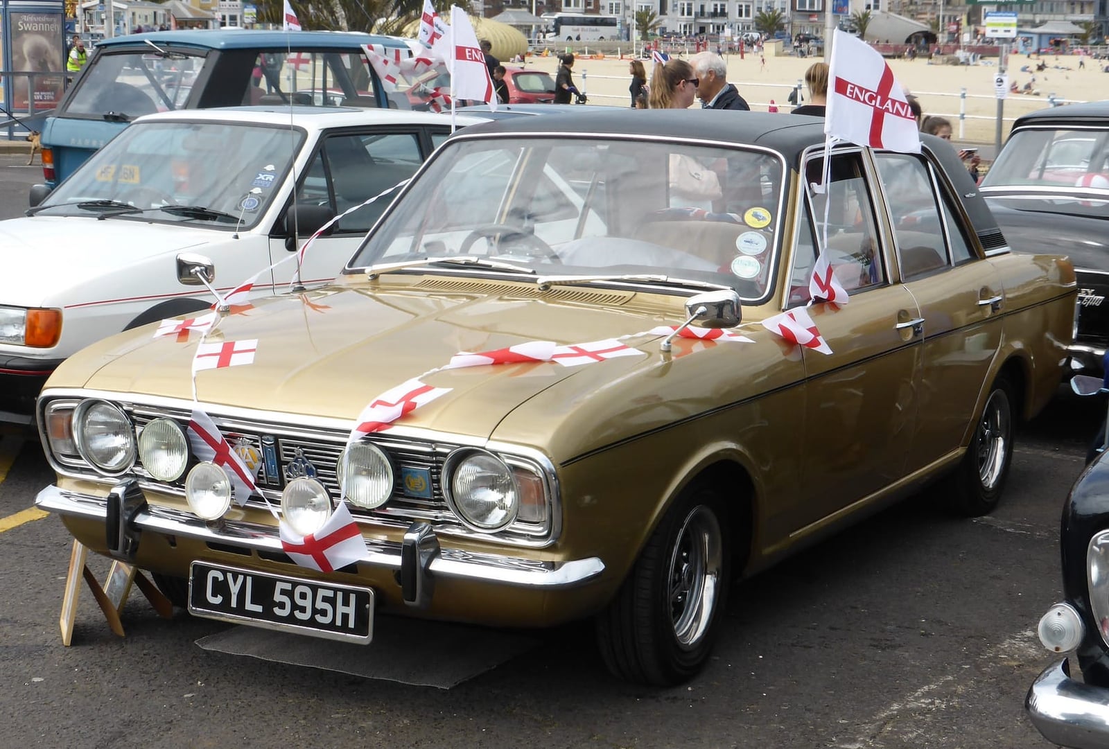 A gold 1970 Ford Cortina 1600E decorated with England flags at a seafront show, UK registration CYL 595H