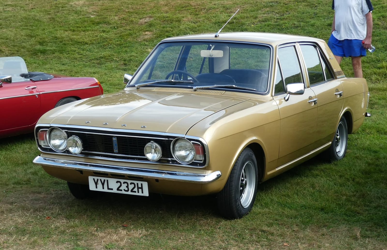 A gold 1970 Ford Cortina 1600E on grass at a classic car show, front three-quarter view, UK registration YYL 232H