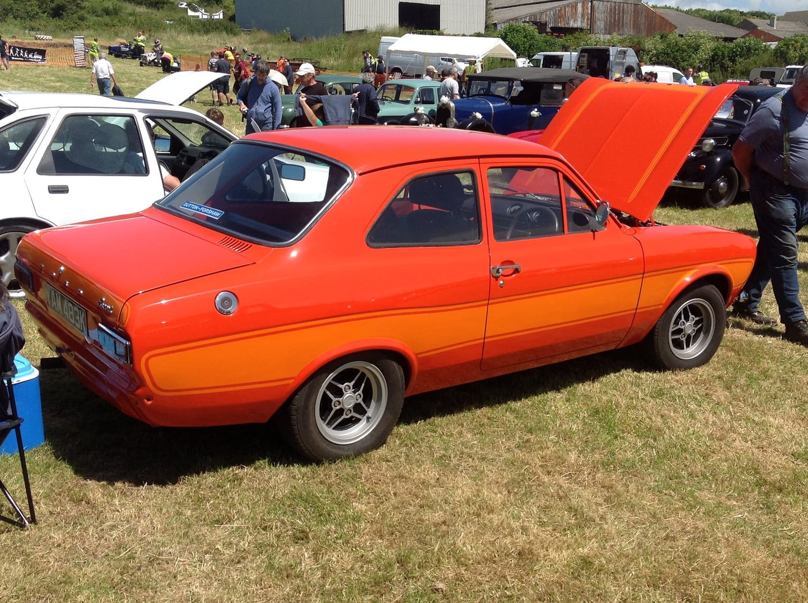 A red 1972 Ford Escort Mk1 1300 L dressed as a Mexico, with its bonnet raised at a show