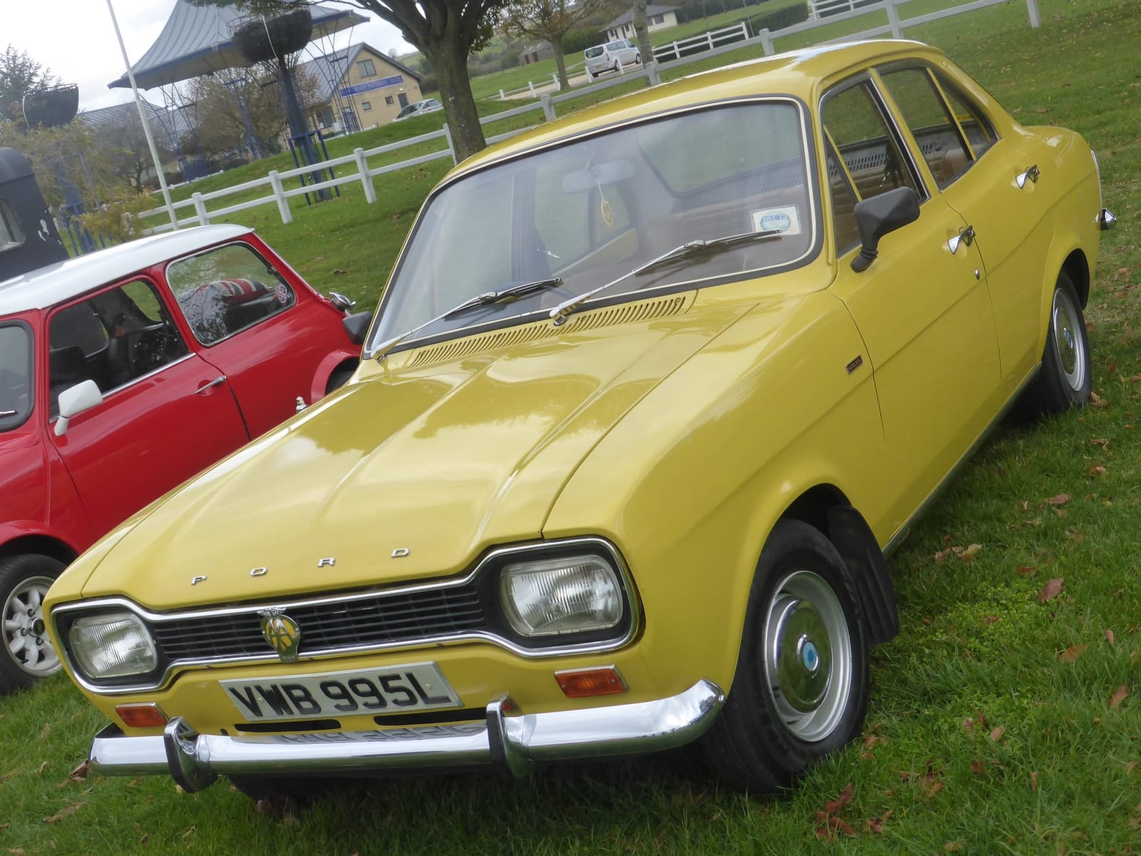 A yellow 1973 Ford Escort Mk1 1300 XL four-door saloon with a UK registration on a show field