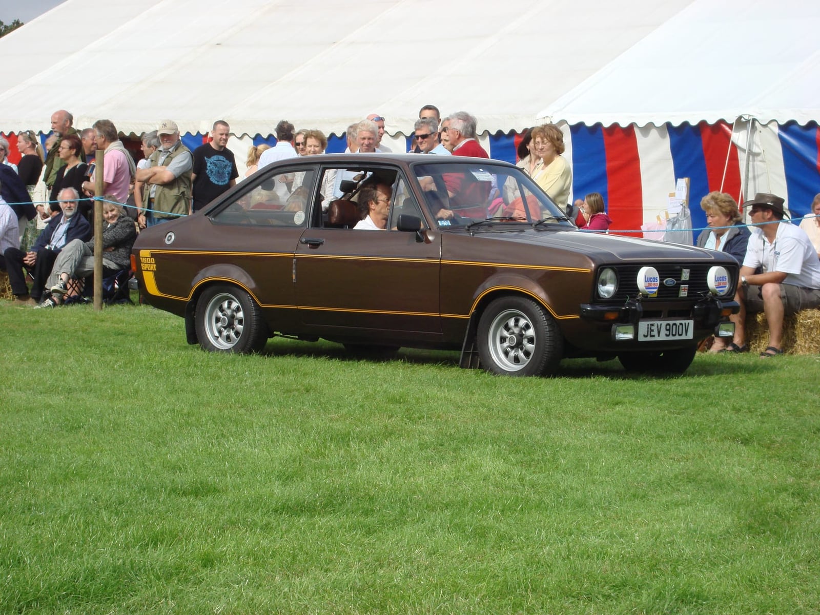 A brown Ford Escort Mk2 1600 Sport two-door at a classic car show, front three-quarter view, UK registration JEV 900V