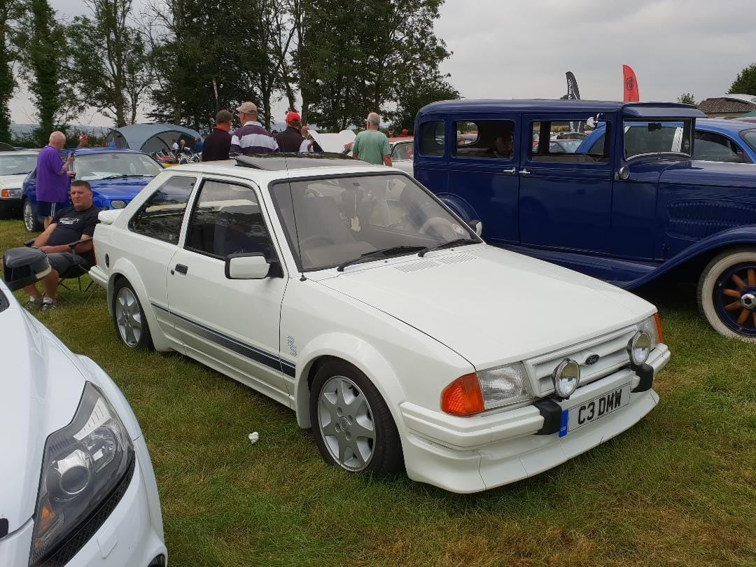 A white 1985 Ford Escort RS Turbo Series 1 with a UK registration on a show field