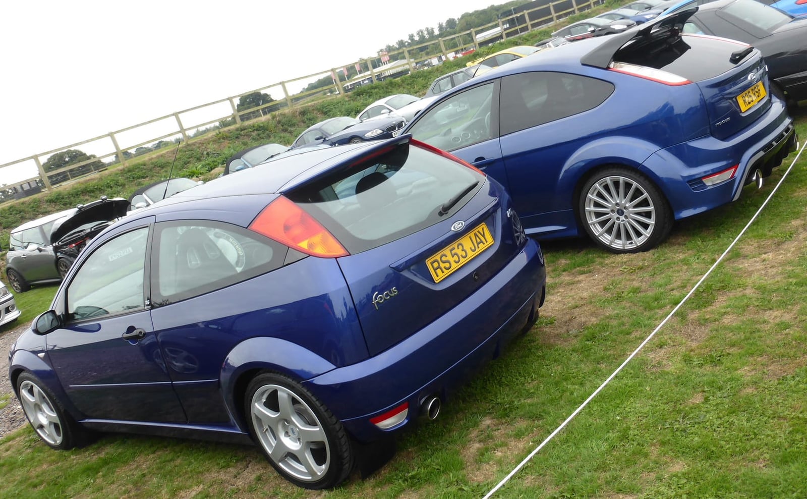 A Mk1 and a Mk2 Ford Focus RS, both blue, parked together on a show field