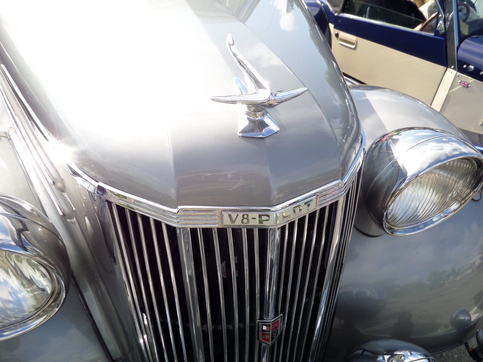Close-up of a Ford V8 Pilot grille and headlamp showing the V8 Pilot badge on the bonnet