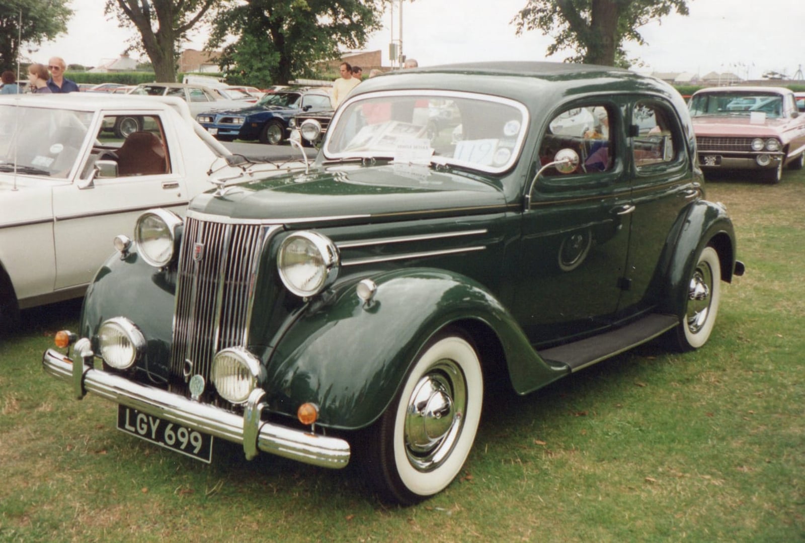 A dark green 1950 Ford V8 Pilot on grass at a classic car show, front three-quarter view, UK registration LGY 699