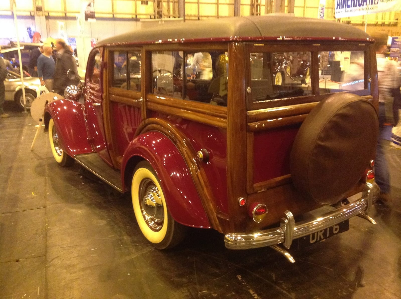 A red and timber 1953 Ford V8 Pilot woodie estate on indoor display, rear three-quarter view with rear-mounted spare wheel, UK registration URT 6