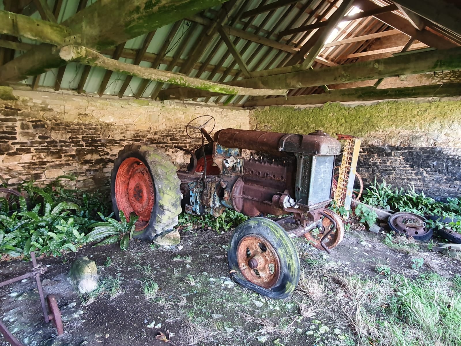 A rusty Fordson Major standing on earth inside a derelict barn