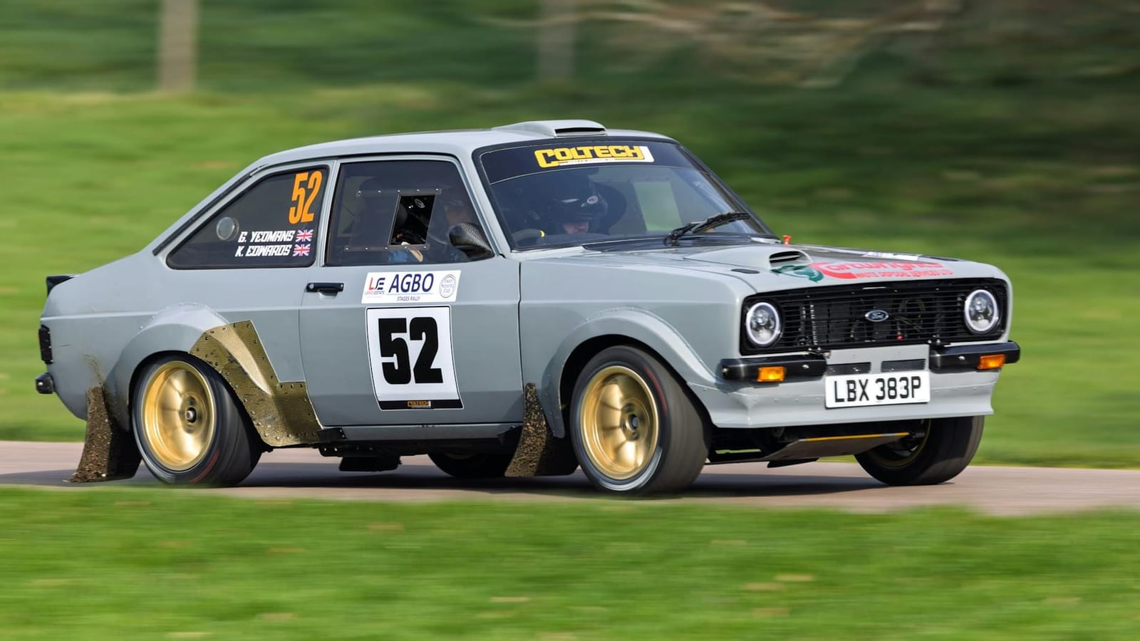 A grey Ford Escort Mk2 rally car, number 52 on gold wheels with flared arches, sliding through a corner