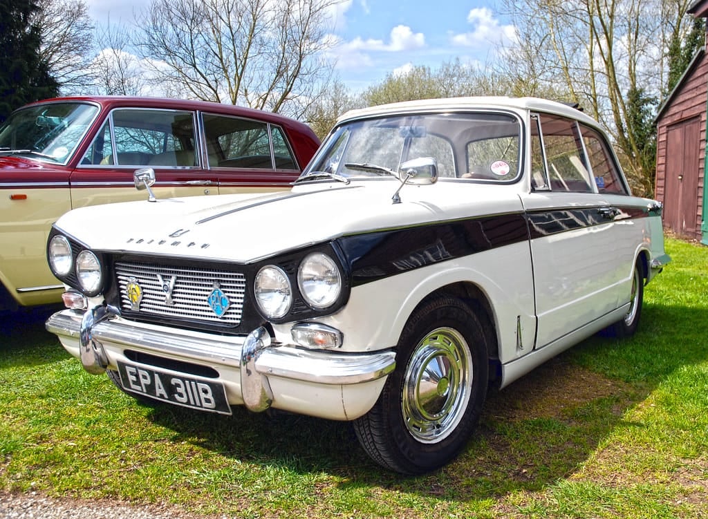 A white and black two-tone Triumph Vitesse on grass at a classic car show, front three-quarter view, UK registration EPA 311B