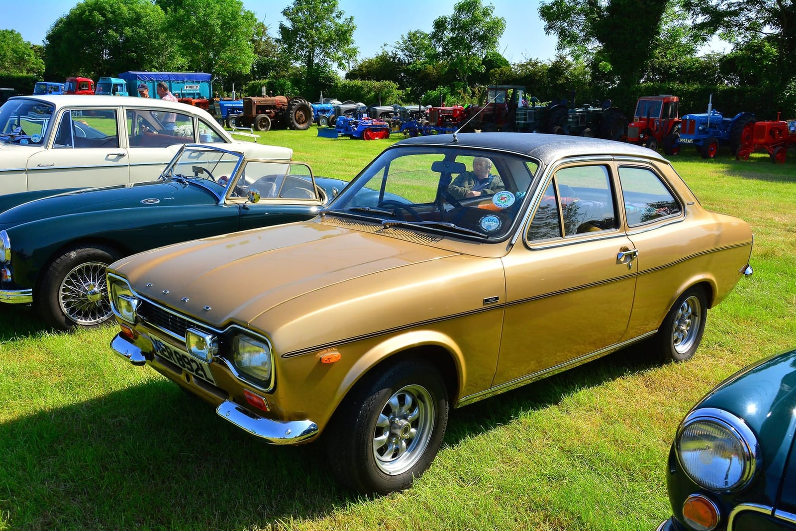 A gold Ford Escort Mk1 two-door on grass at a country fair, front three-quarter view