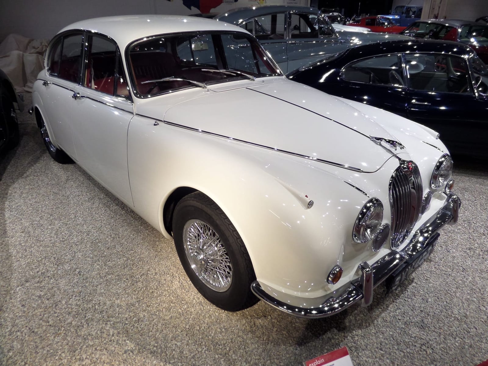 A white 1968 Jaguar 240 saloon displayed indoors at a classic car show