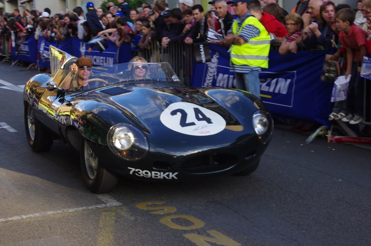 A green Jaguar D-Type racing number 24 passing a packed crowd at Le Mans, UK registration 739 BKK