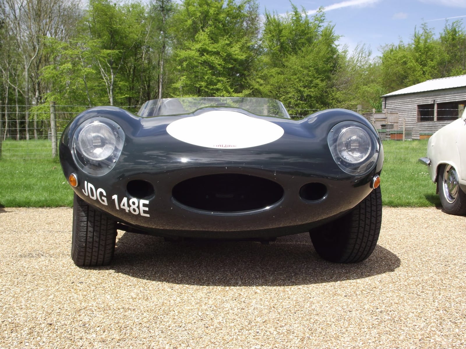 A dark green Jaguar D-Type photographed head-on outdoors, showing the oval air intake and headrest fin, UK registration JDG 148E