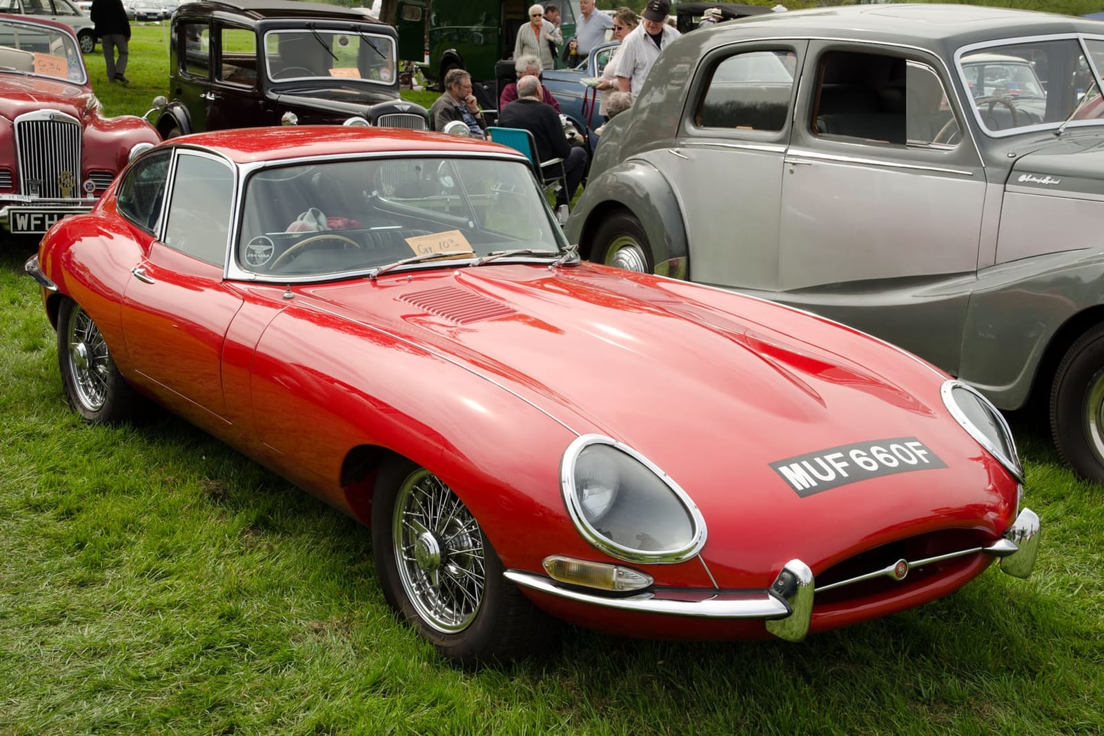 A red 1967 Jaguar E-Type Series 1 fixed-head coupe with UK registration MUF 660F among pre-war cars at a show