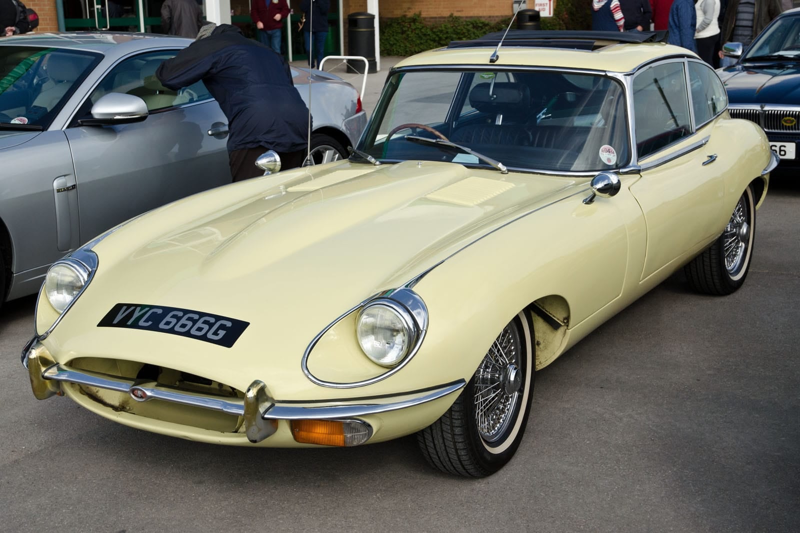 A primrose 1969 Jaguar E-Type Series 2 2+2 coupe at a classic car show, front three-quarter view, UK registration VYC 666G